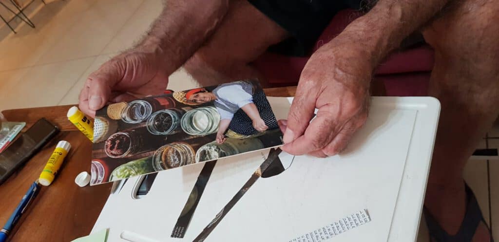 אדם מחזיק תצלום של אישה המביטה מטה לעבר אוסף צנצנות זכוכית.