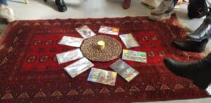 הקלפים מסודרים במעגל סביב נר קטן המונח על מחצלת קלועה, המונחת על שטיח אדום מעוטר בדוגמאות ומוקפת ברגלי האנשים.