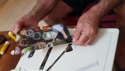 אדם מחזיק תצלום של אישה המביטה מטה לעבר אוסף צנצנות זכוכית.