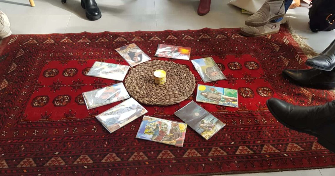 הקלפים מסודרים במעגל סביב נר קטן המונח על מחצלת קלועה, המונחת על שטיח אדום מעוטר בדוגמאות ומוקפת ברגלי האנשים.